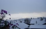 Foto: verschneite Dächer, weiß leuchtende Berge, tiefe graue Wolke