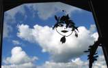 Foto: ein Gesicht aus Lorbeerblättern am Fenster. Die Cumuluswolken sehen wie ausgebreitete Flügel aus.