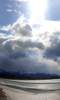 Foto: glitzernde Forggenseearme, darüber Schauerwolken, darüber die Sonne