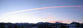 Foto: fast wolkenloser Alpenrand, roter Kondensstreifen