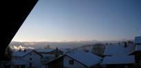 Foto: morgens lugen die höchsten Bergspitzen aus einer Wolkenbank, der übrige Himmel ist blau, die Rauchfahnen leuchten im ersten Sonnenlicht